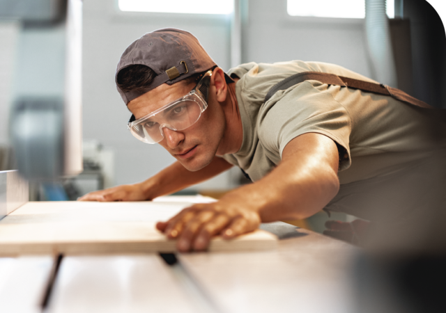 man with safety glasses lining a sheet of wood up for cutting on a table saw