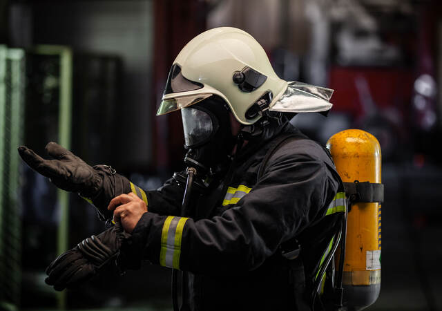 firefighter portrait wearing full equipment with oxygen mask. Putting on protective gloves. Fire trucks in the background.