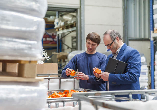 Two people inspecting a batch of orange plastic parts inside a warehouse