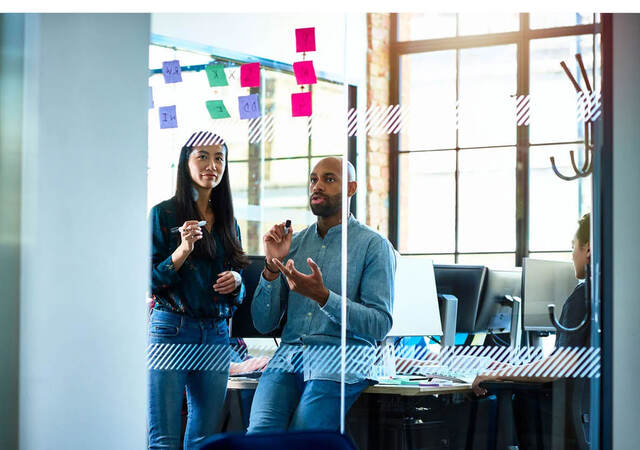 Two people putting sticky notes on a wall