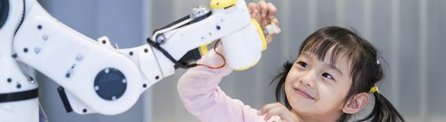 A young girl looking at a robotic arm.