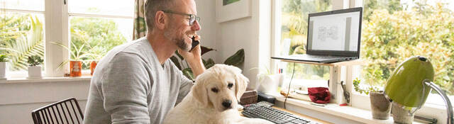 Person smiling and working from home with cute yellow puppy on their knee