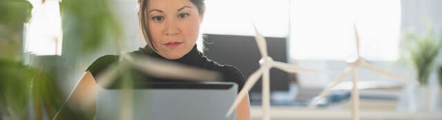 a person with small wind turbine models on a desk, working on a laptop