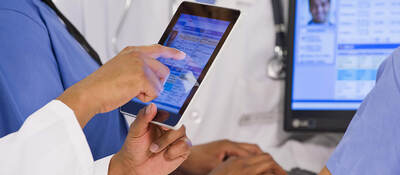 A close-up of a group of four co-workers sharing patient information on tablet and desktop screens