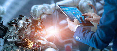 Person using tablet to control robotic arm in a factory