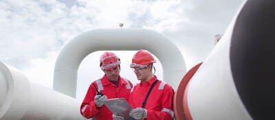 Two engineers having a discussion in front of pipes at a gas storage plant