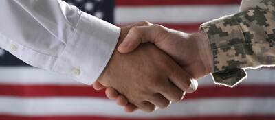 Military personnel shaking hands in front of an American flag