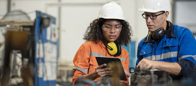 Two manufacturing process engineers in a factory looking at a tablet together.  