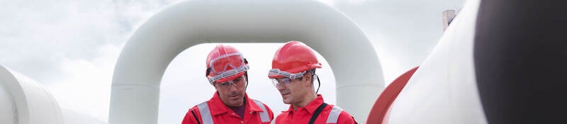 Two engineers having a discussion in front of pipes at a gas storage plant