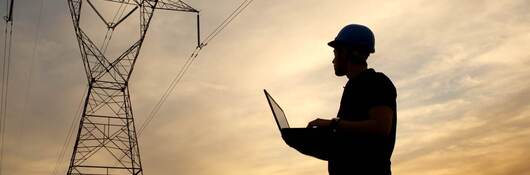 Electrical engineer while working laptop while looking at a power station at dusk