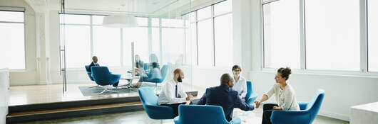 Business professionals sitting in blue chairs having a meeting in a white, modern office
