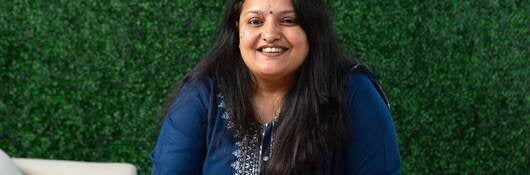 Rohini Poonacha in blue shirt in front of green leafy wall. 