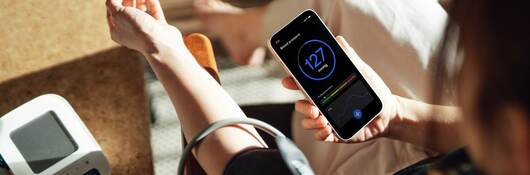 Elevated view of woman checking her blood pressure with a blood pressure monitor and mobile app on smartphone