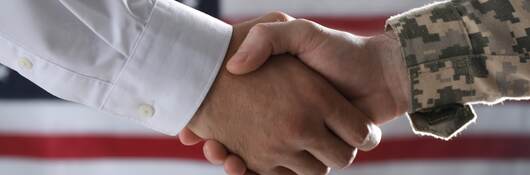 Military personnel shaking hands in front of an American flag