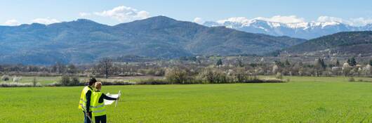 Two engineers looking at plans for a wind farm while standing in a large, open valley