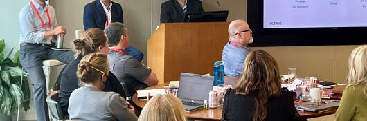 Three speakers at a podium presenting to a room of people