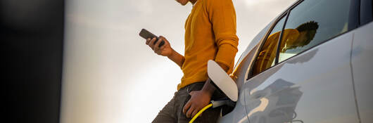 A young person leaning against a car and looking at a mobile device