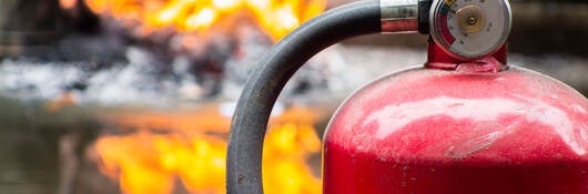 Fire extinguisher in foreground with flames in background