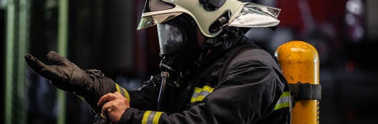 firefighter portrait wearing full equipment with oxygen mask. Putting on protective gloves. Fire trucks in the background.