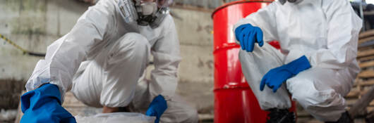 Two chemists wearing PPE recover a chemical spill on a factory warehouse floor