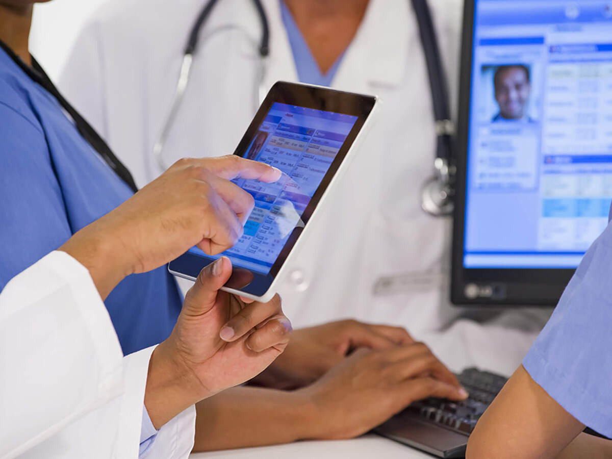 A close-up of a group of four co-workers sharing patient information on tablet and desktop screens