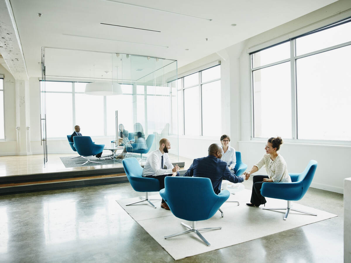 Business professionals sitting in blue chairs having a meeting in a white, modern office