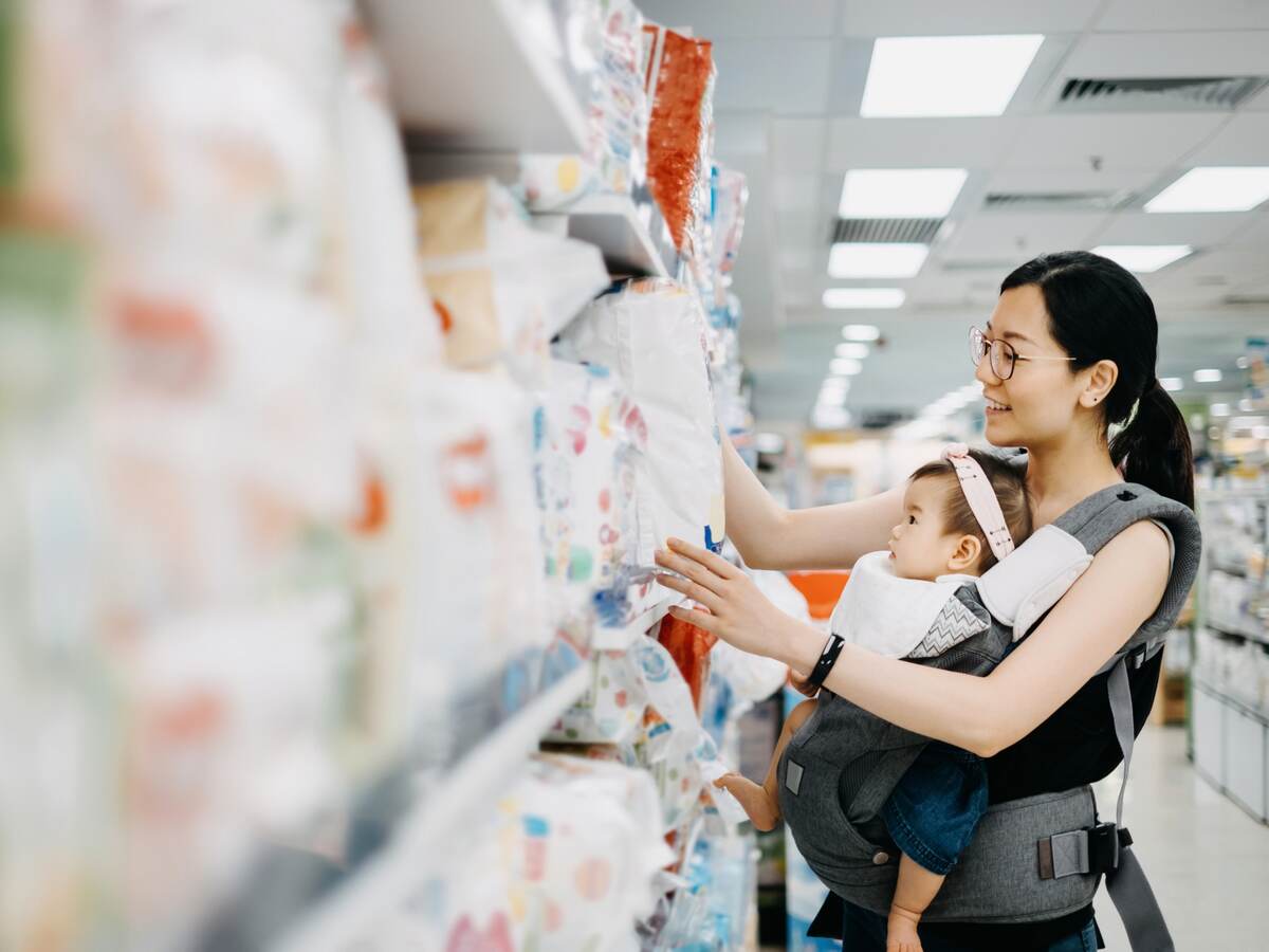 Young Asian mother carrying cute baby girl shopping for baby product in a shopping mall and is looking at a variety of diapers.