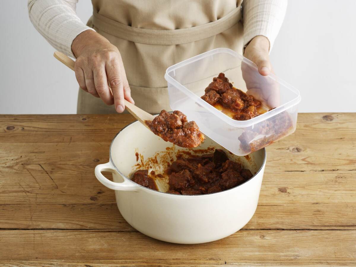 Woman spooning food into a plastic container.