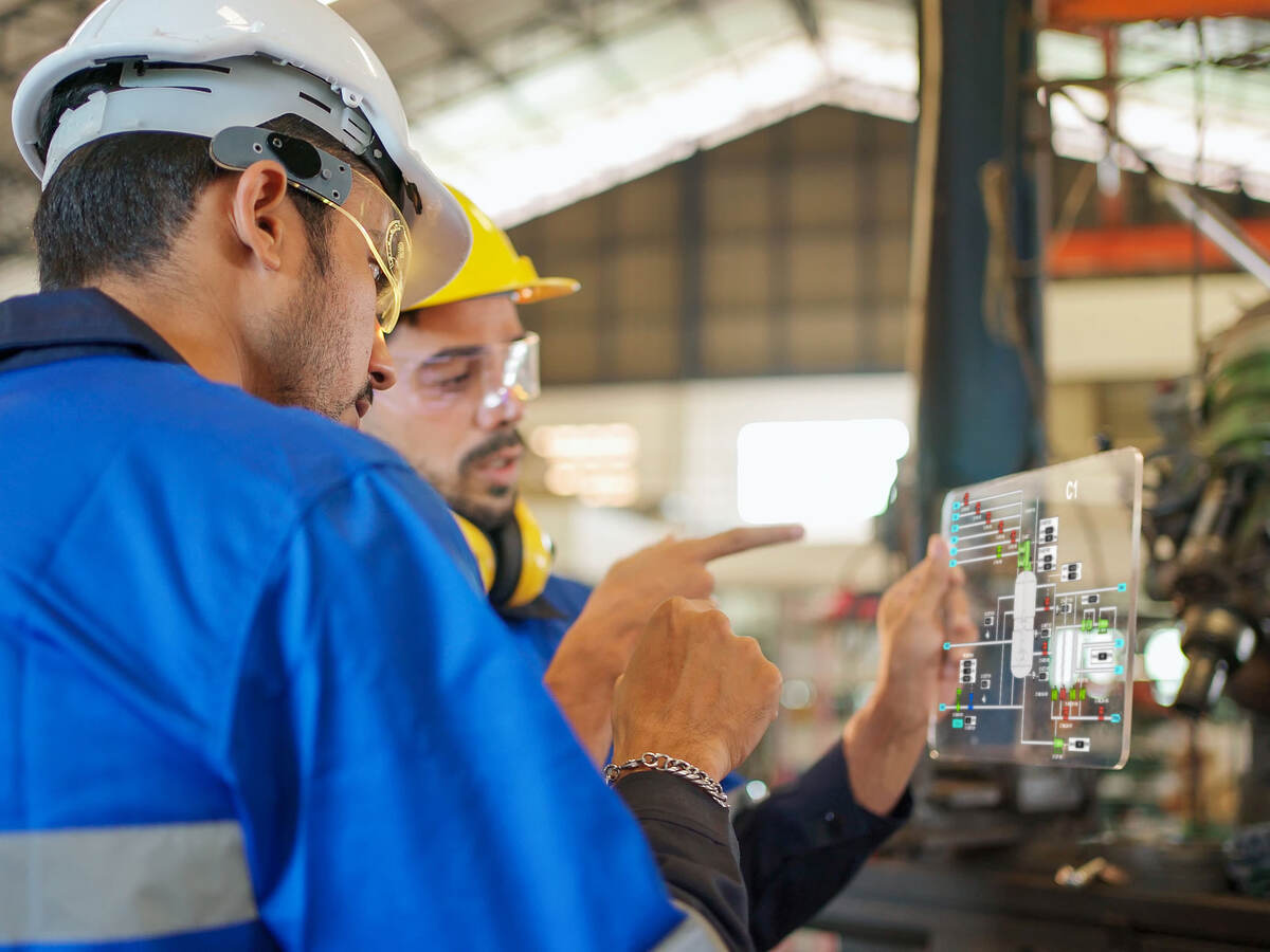 Two engineers wearing PPE and working on a futuristic tablet