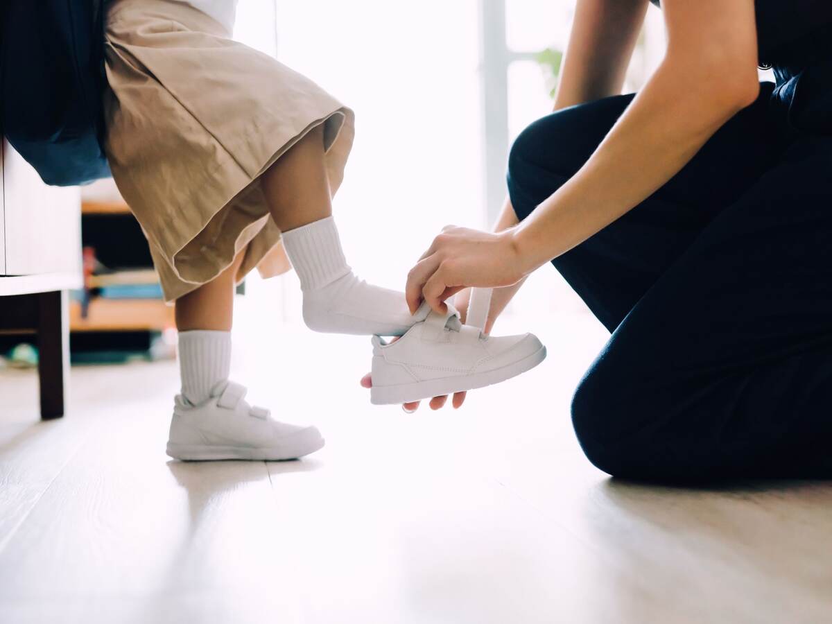 Mother putting on shoes for her daughter.