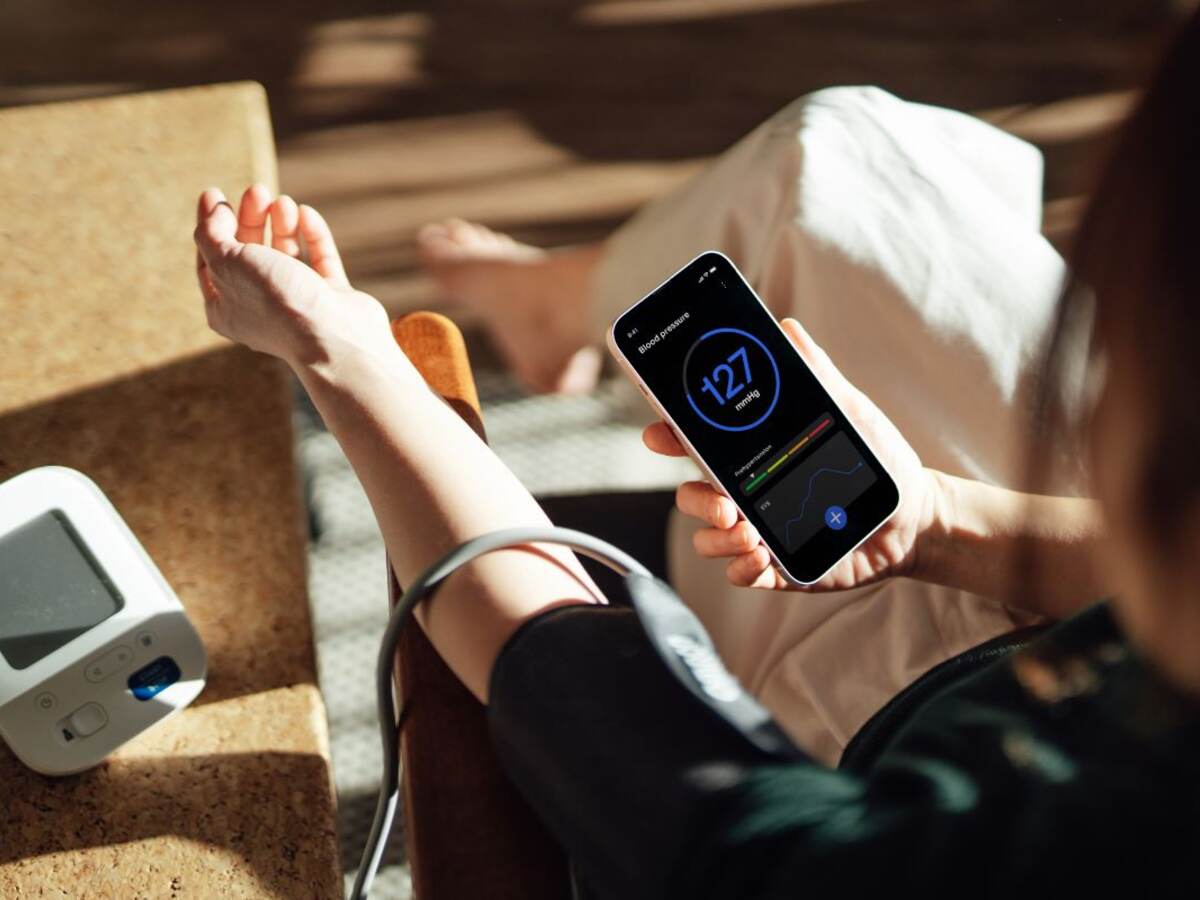 Elevated view of woman checking her blood pressure with a blood pressure monitor and mobile app on smartphone