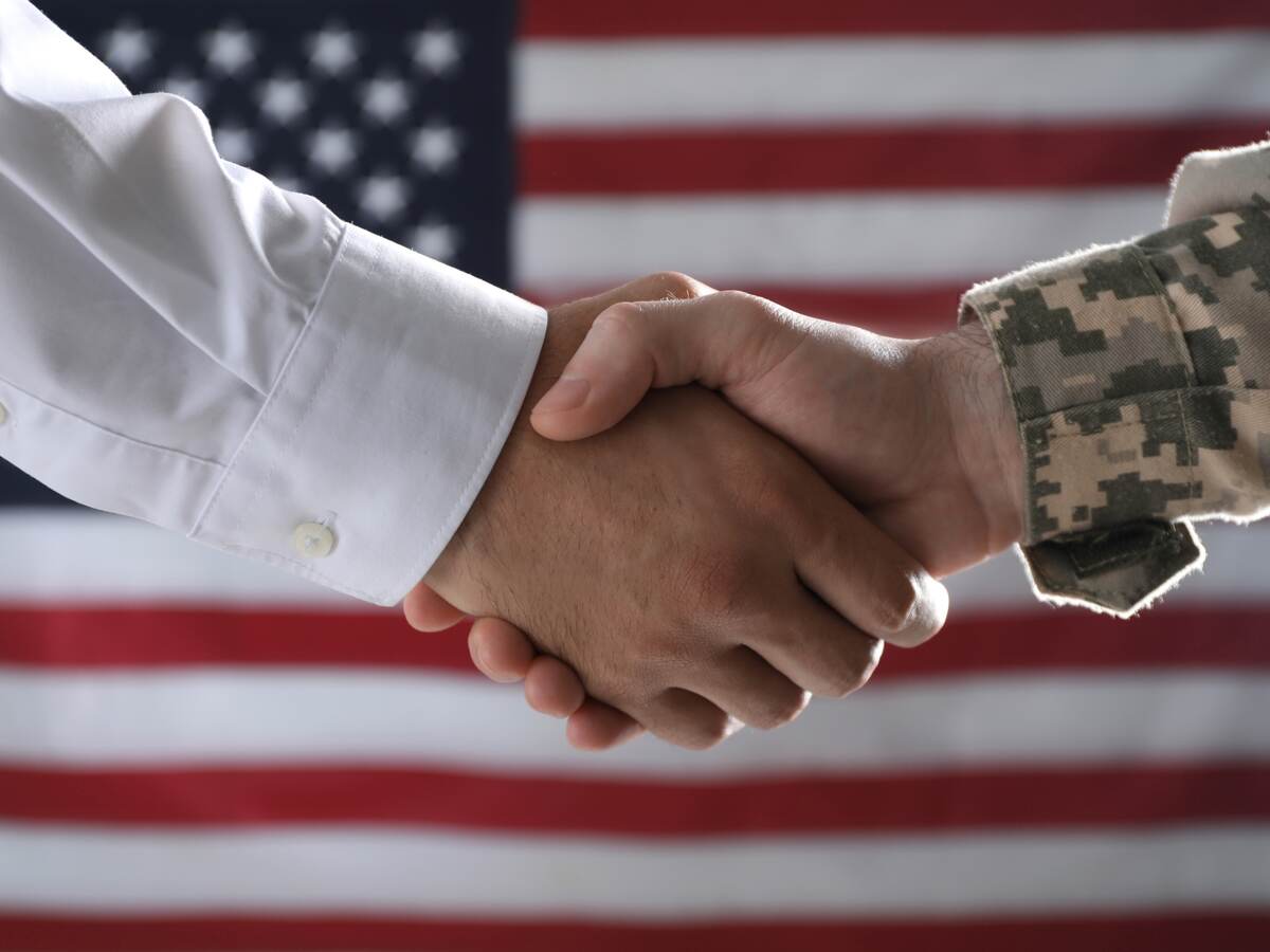 Military personnel shaking hands in front of an American flag