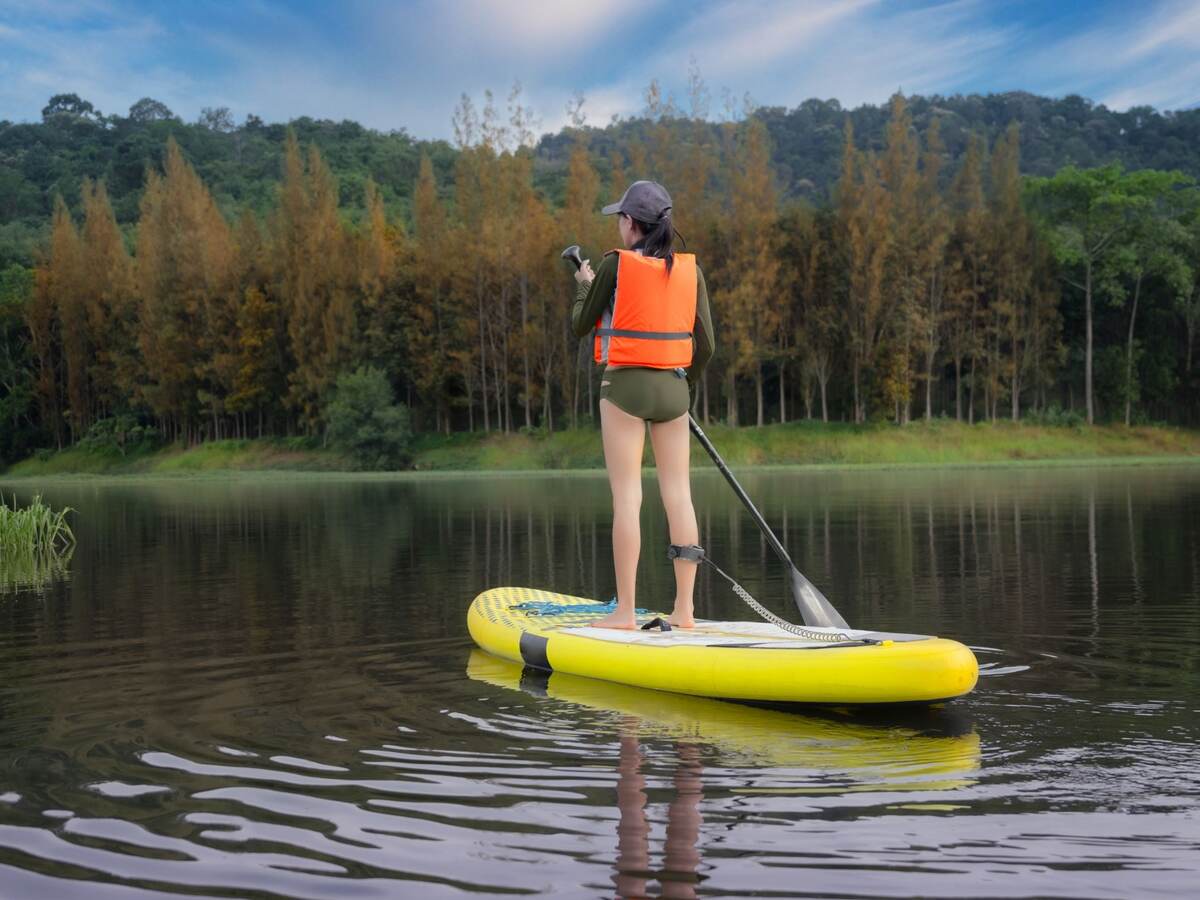 Young woman enjoying paddleboarding in mountain lake wearing short wetsuit and an orange life jacket.