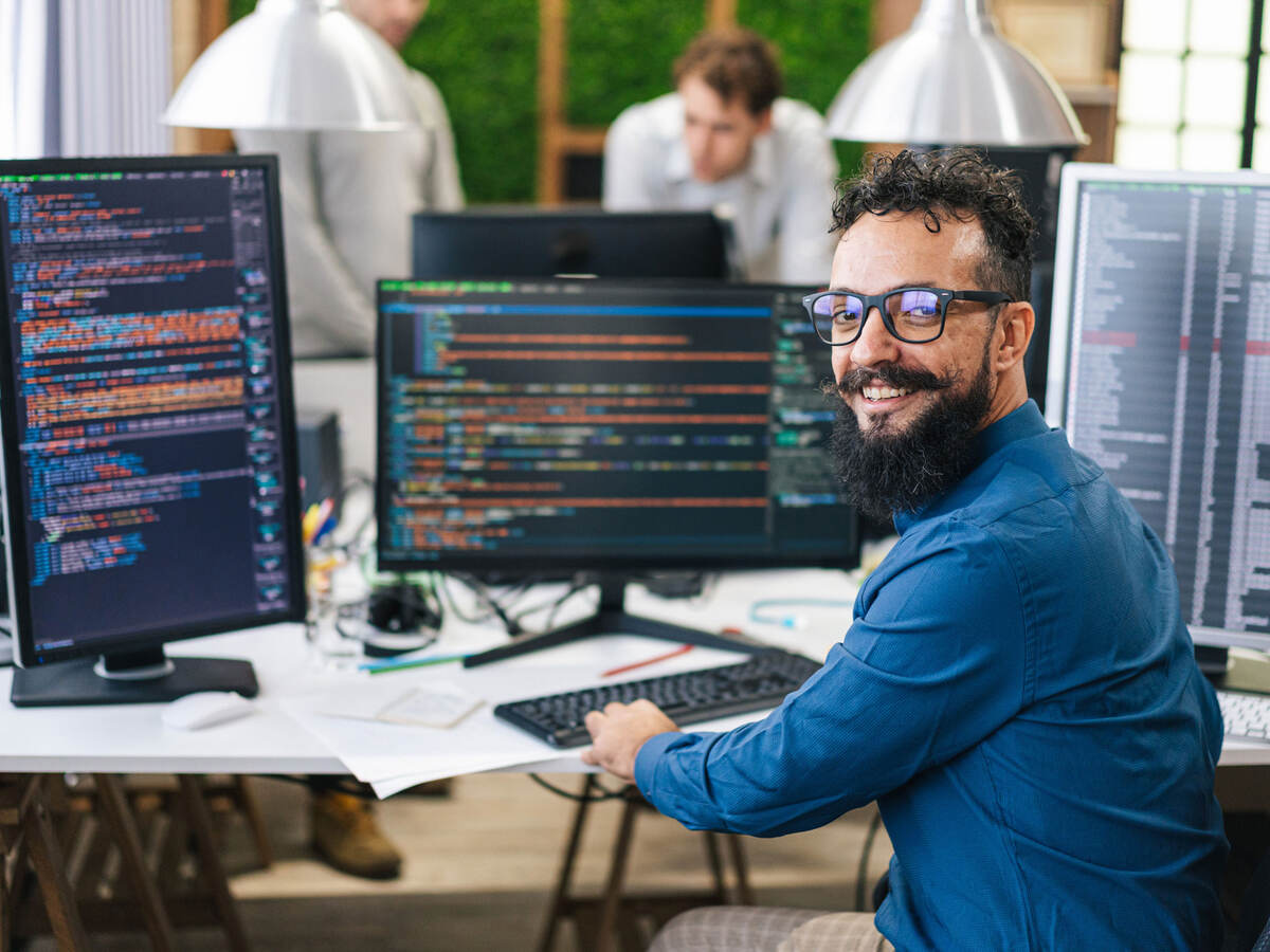 A happy person surrounded by multiple monitors