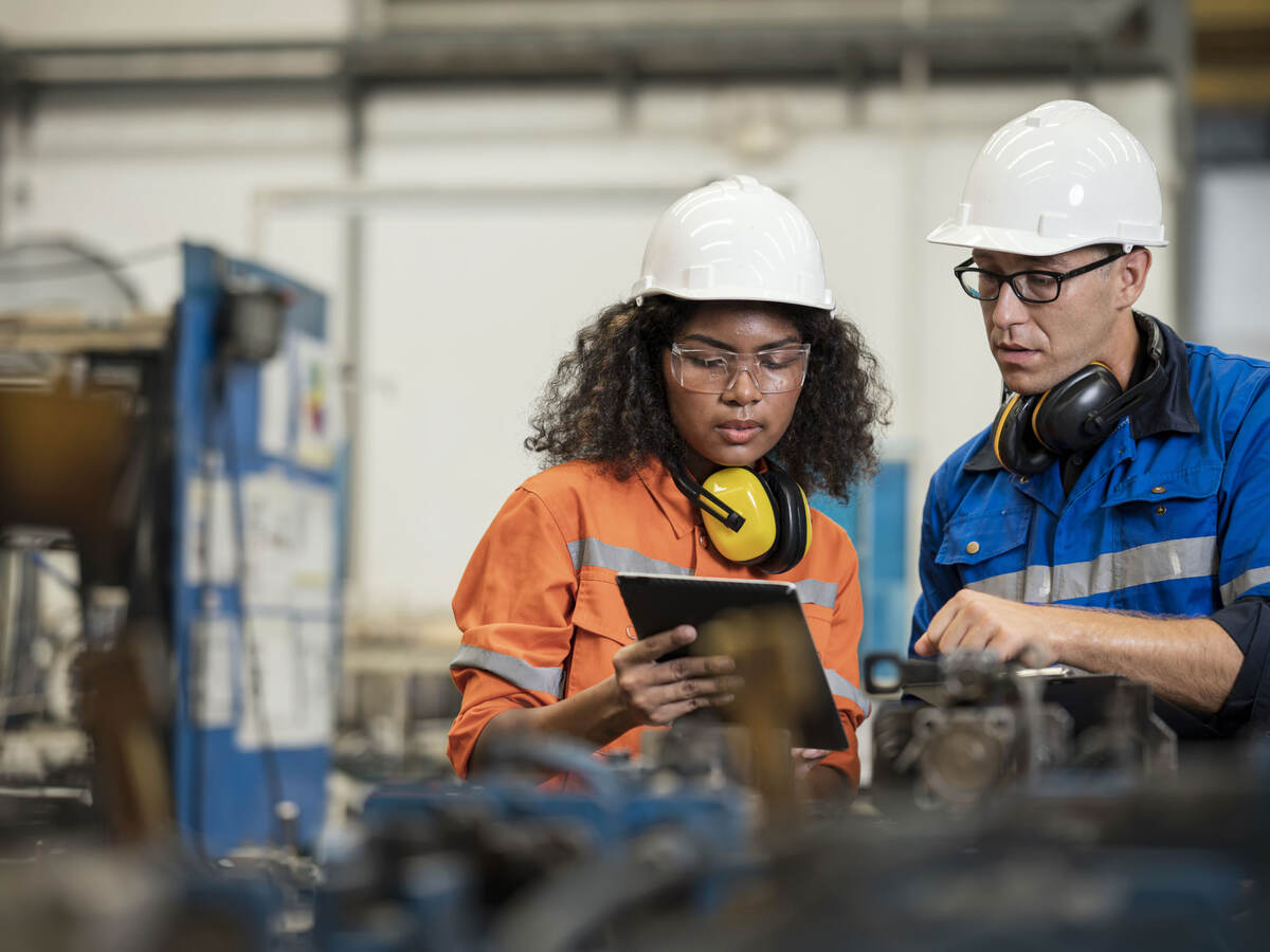 Two manufacturing process engineers in a factory looking at a tablet together.  