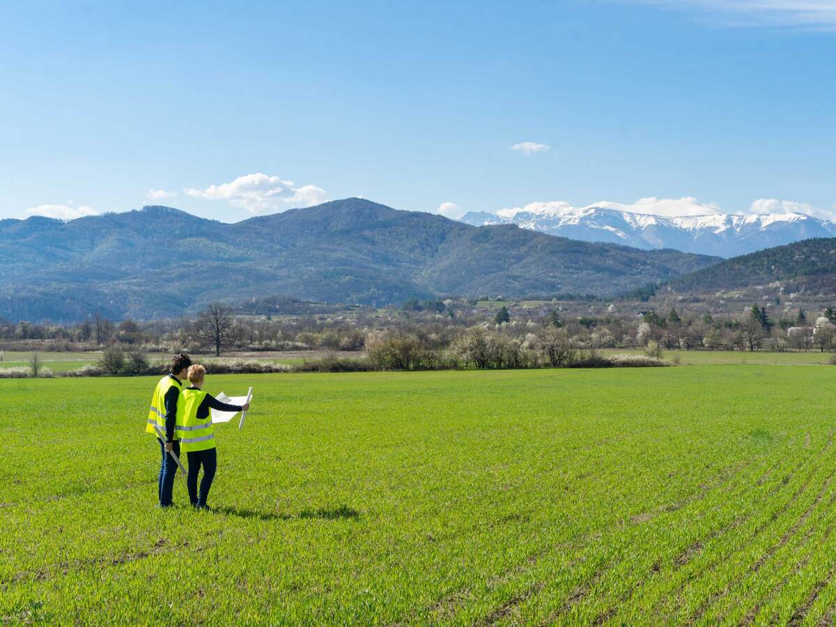 Two engineers looking at plans for a wind farm while standing in a large, open valley