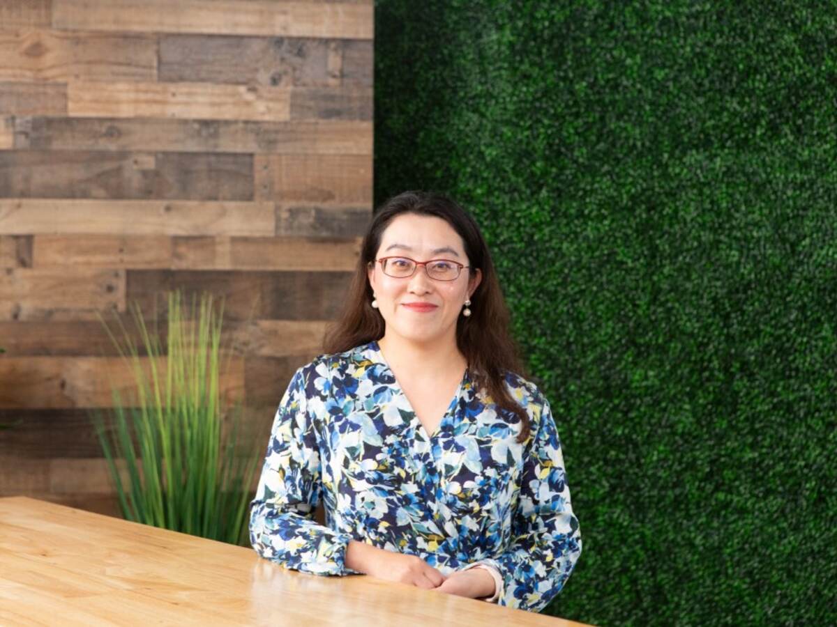 Vicky Zhang in floral shirt sits at table in front of vine covered wall. 