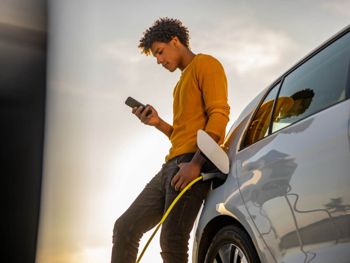 A young person leaning against a car and looking at a mobile device