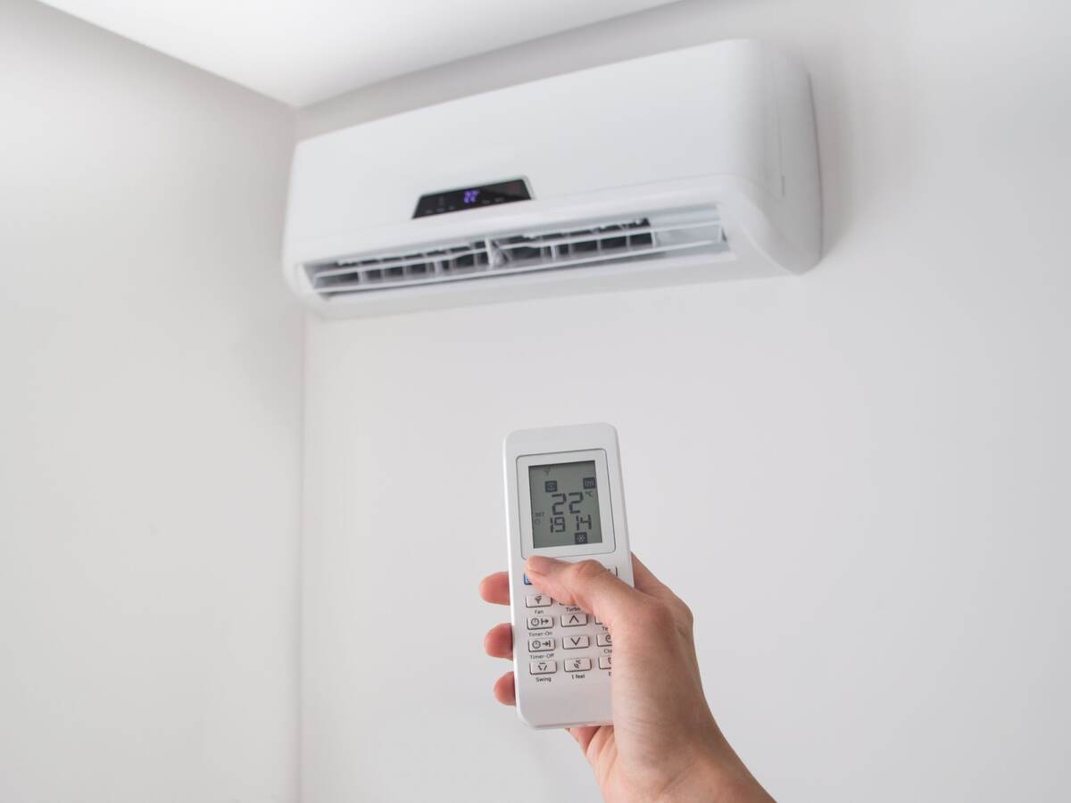 Hand holding remote control for air conditioner on white wall