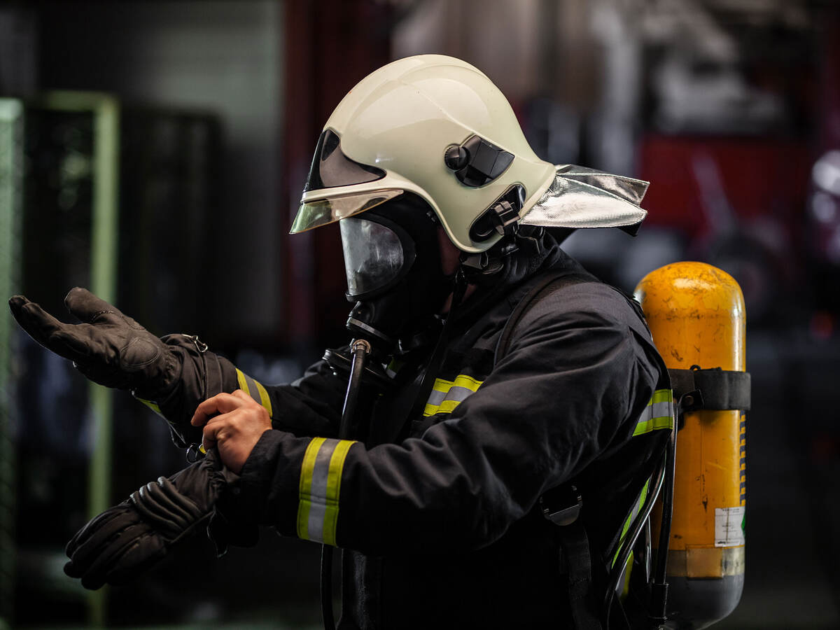 firefighter portrait wearing full equipment with oxygen mask. Putting on protective gloves. Fire trucks in the background.