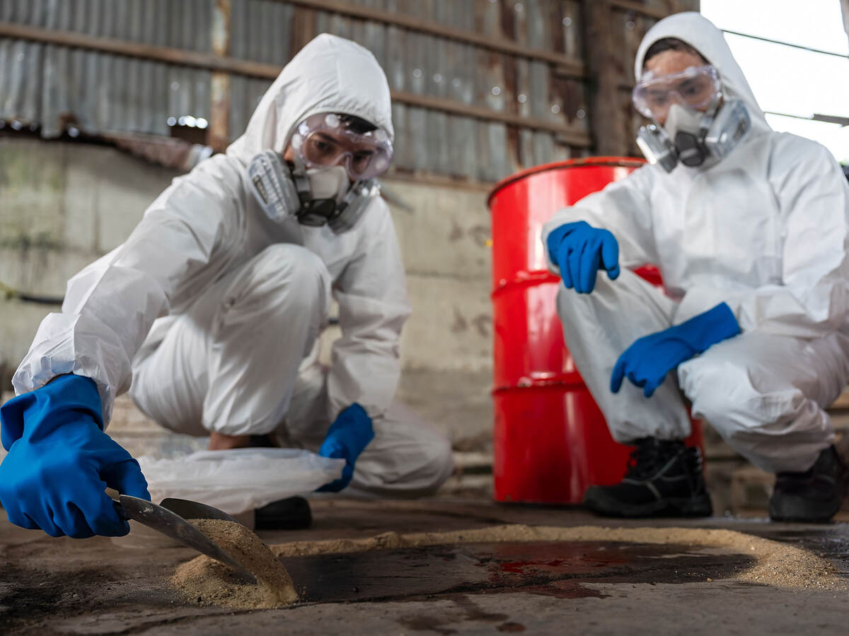 Two chemists wearing PPE recover a chemical spill on a factory warehouse floor